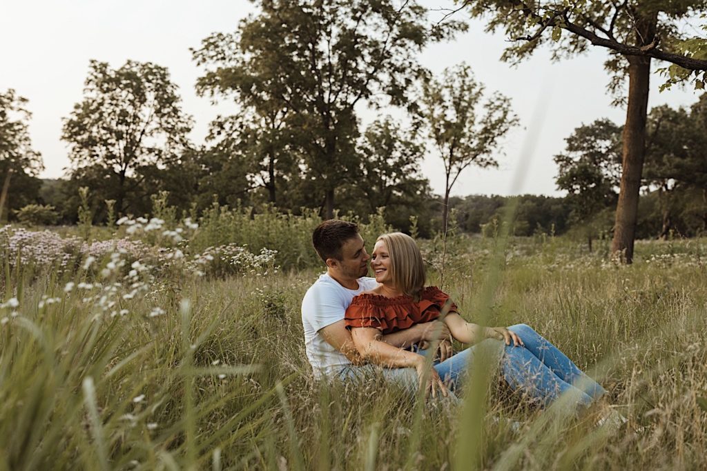 Woman sitting on a mans lap while seated in a field looking at one another in a Wisconsin forest preserve