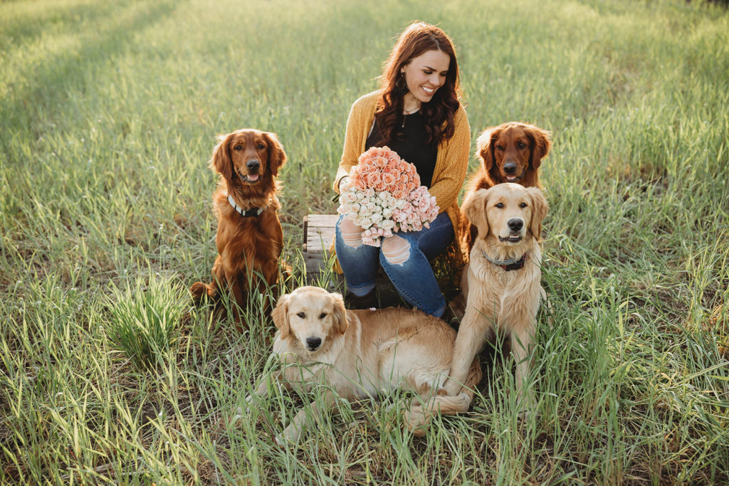 Florist Joey of Remington Flowers & Co holding flowers in a field surrounded by her 4 golden retrievers