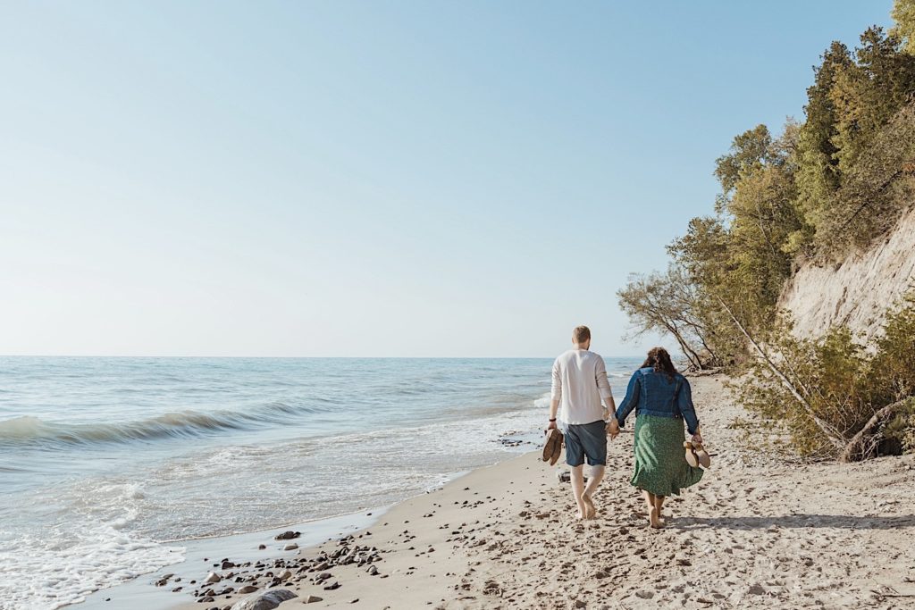 Couple walks along the beach away from the camera at a Wisconsin forest preserve while