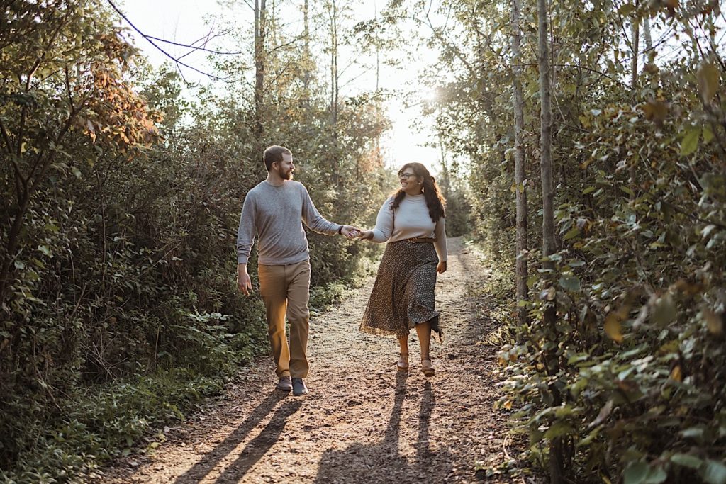 Couple holds hands and look at one another while walking along a path in a Wisconsin  forest preserve