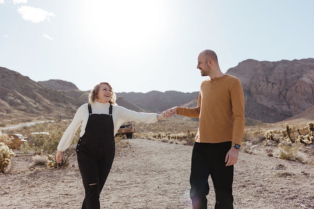 Couple wearing neutral colors holding hands and smiling at one another walking in the desert