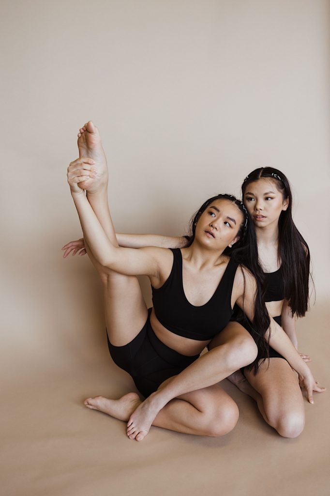 Two dancers wearing all black sit and stretch together