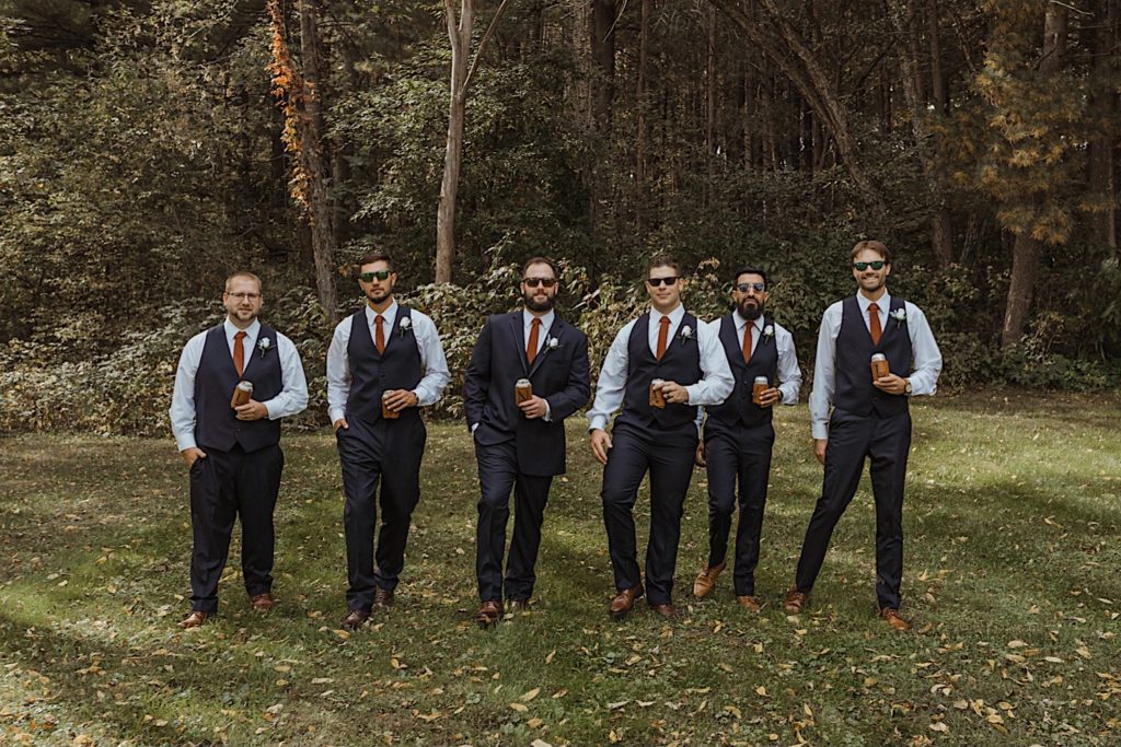 Groom and groomsmen walk towards the camera holding beer and wearing sunglasses