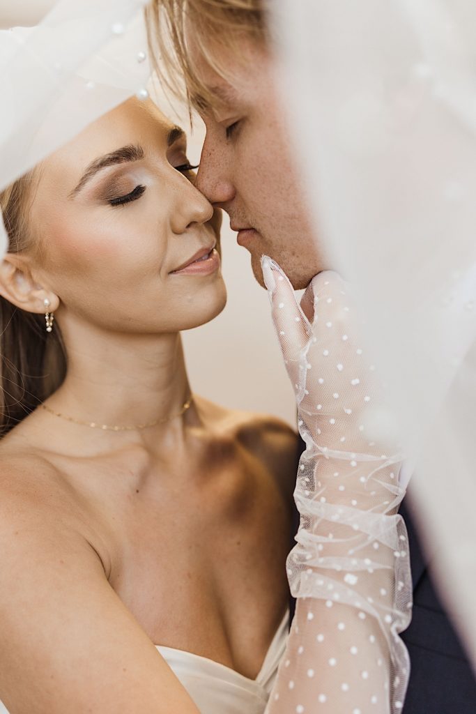 Woman in a wedding dress wearing white gloves about to kiss a man under her veil
