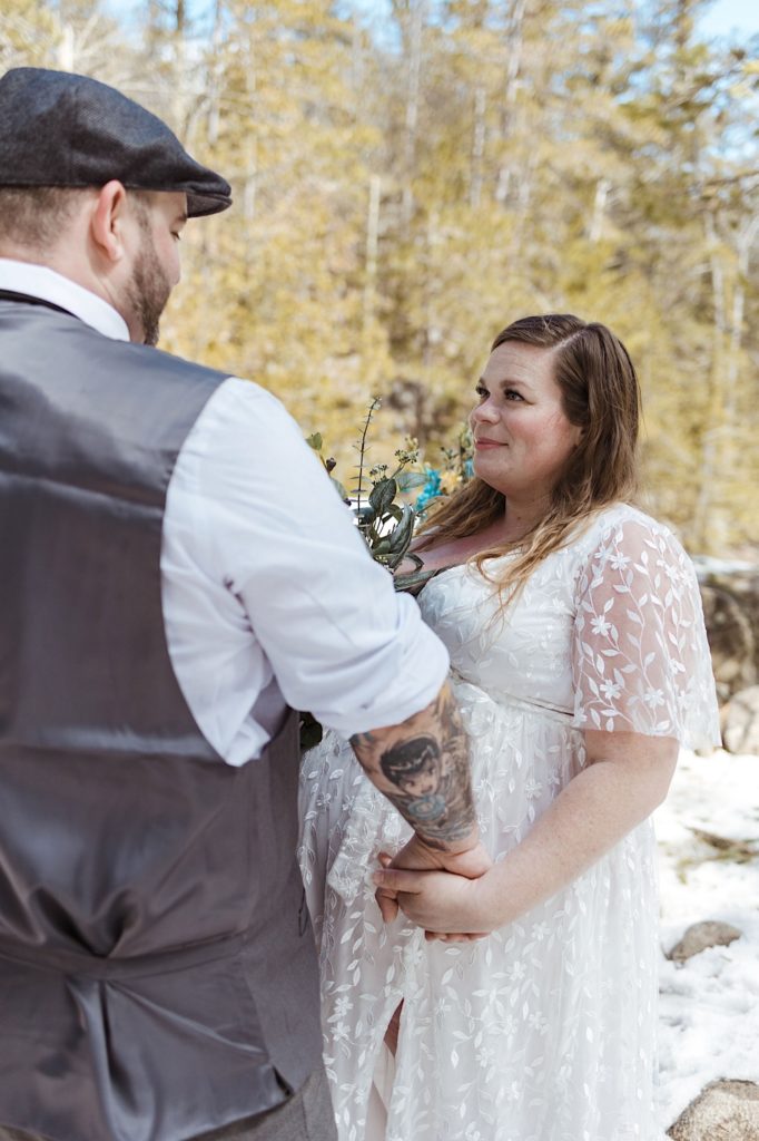 A bride smiles at her husband while they hold hands in a snowy forest