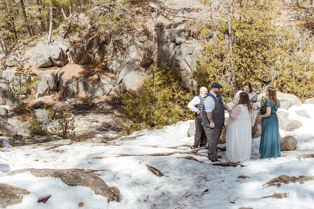 A bride and groom stand on a snowy hill with their guests during their elopement in a Wisconsin forest