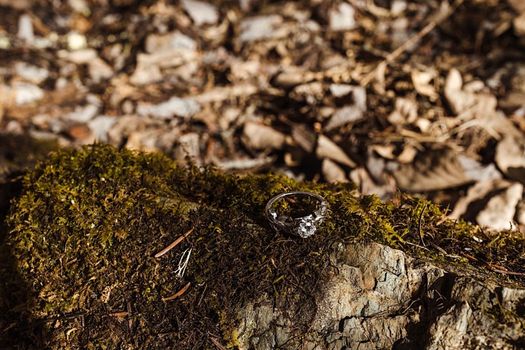 A wedding ring atop a moss covered rock with leaves in the background